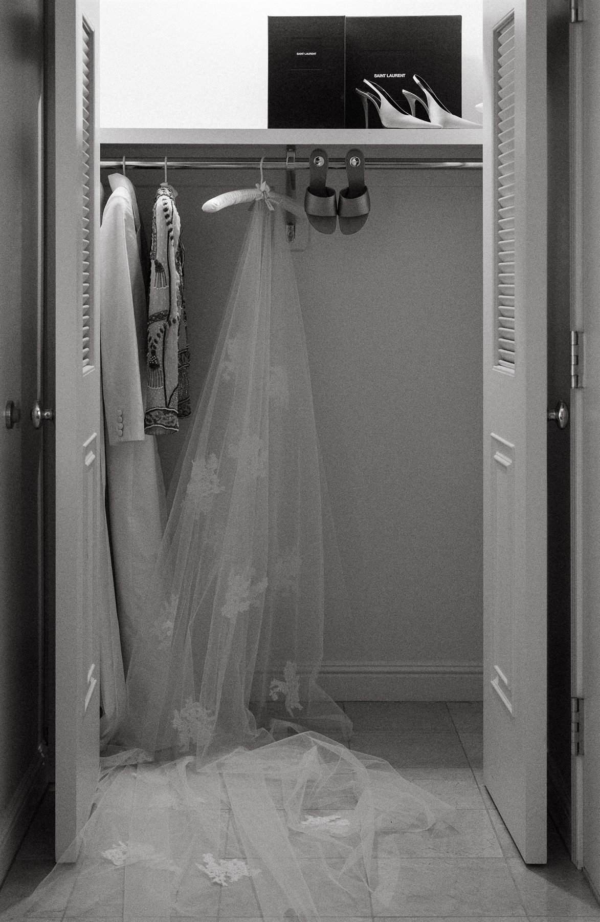 Black-and-white frame of the bride&rsquo;s veil hanging in an open wardrobe beside her Saint Laurent shoes.