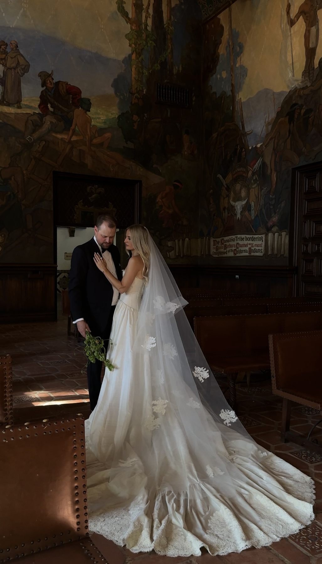 The couple in the Mural Room, the groom in a Tom Ford tuxedo, the bride&rsquo;s train spread across the tile behind them.