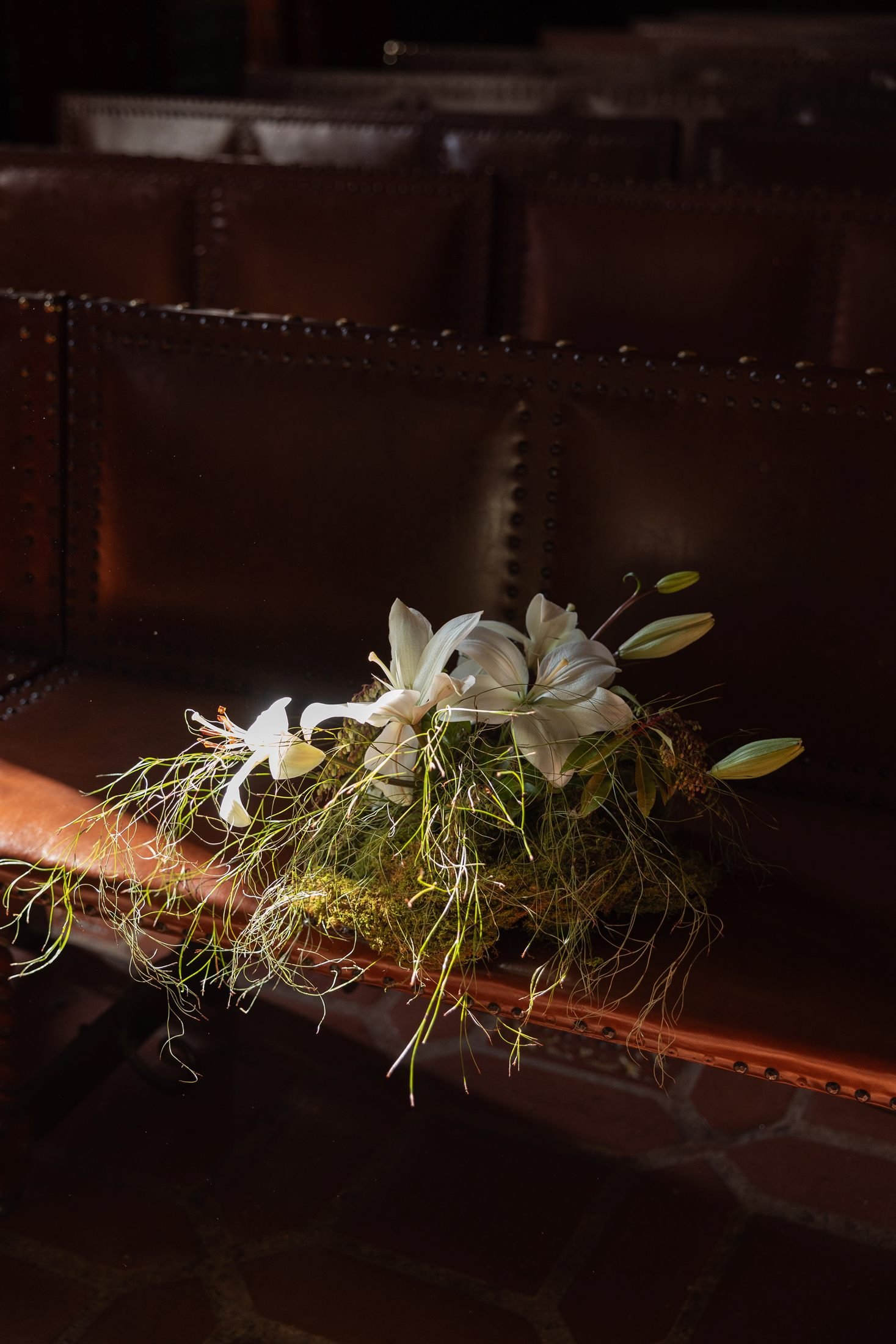 Lilies and tapered candles arranged along a dark wooden bench in the Mural Room.