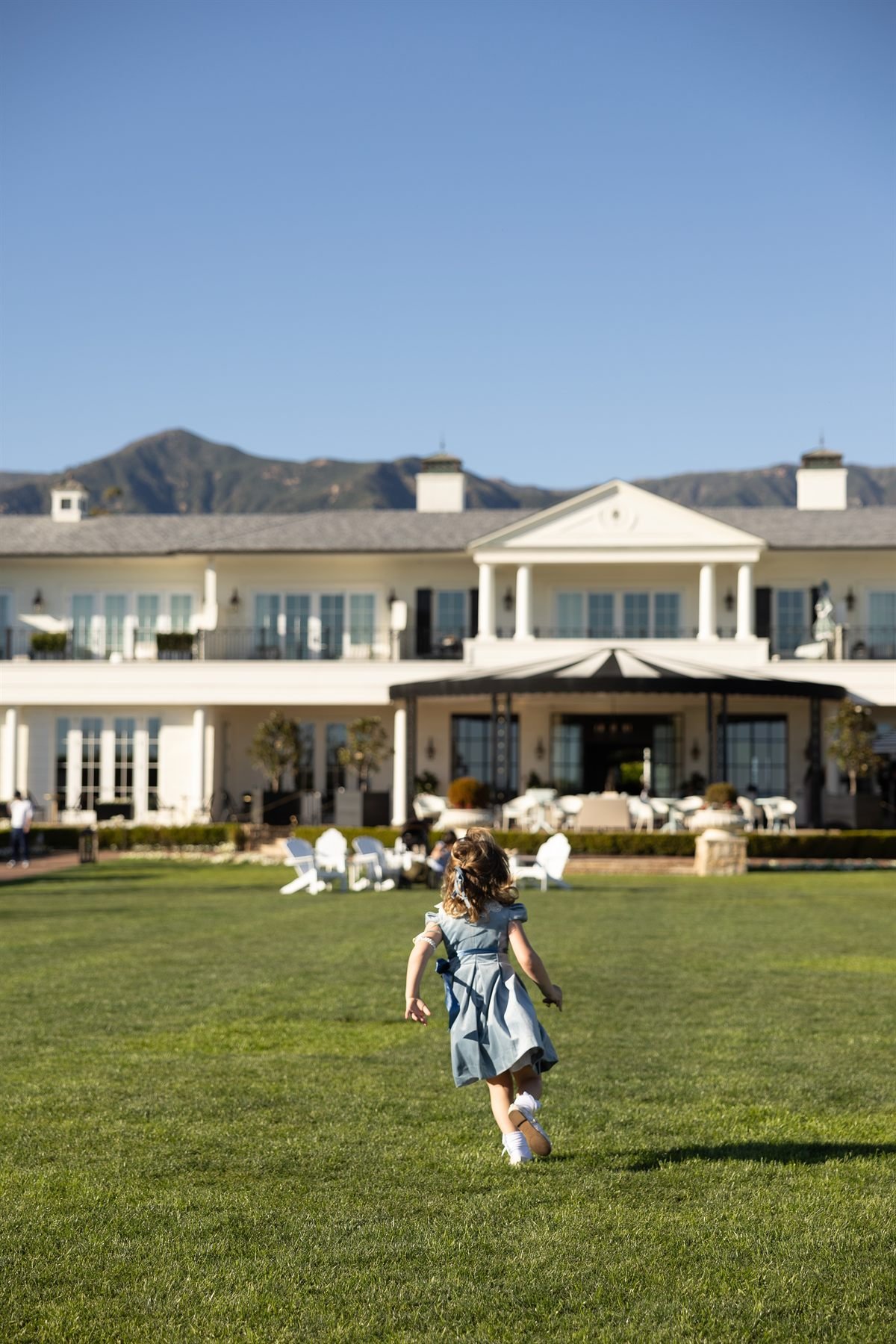 A child running across the lawn at Rosewood Miramar Beach towards the white hotel building at golden hour.