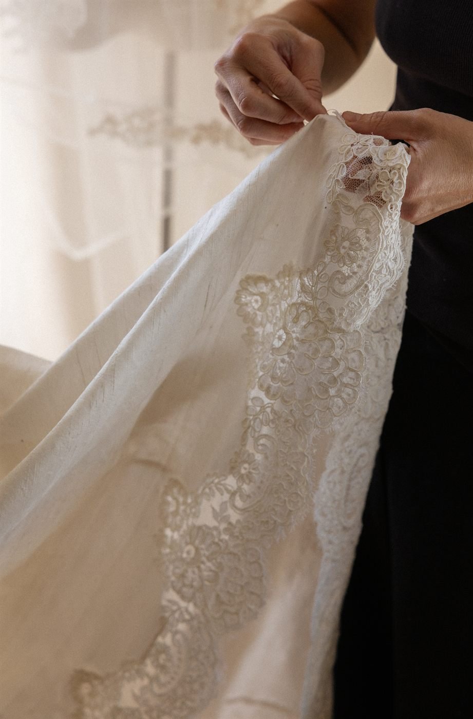 Hands holding a panel of vintage French corded lace against the silk dupioni train of the Montecito gown.